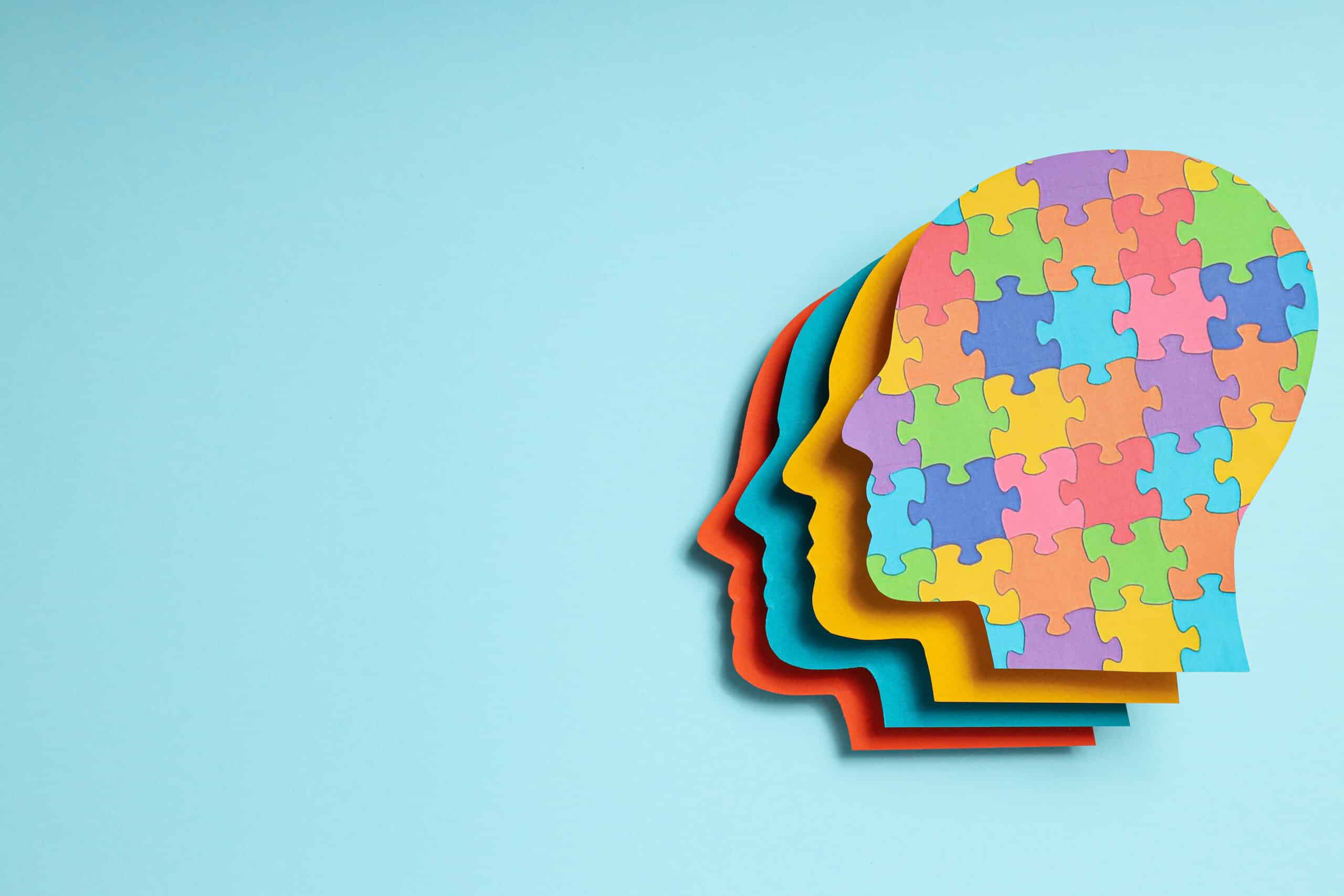 Paper human heads with colorful puzzle pieces on a light background, place for text. World autism day concept
